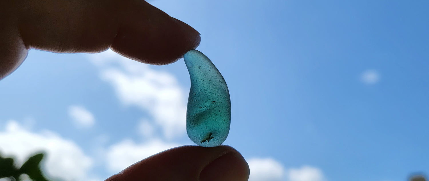 teal and green teardrop shape seaglass held in the blue sky with two fingers