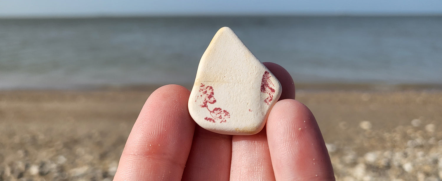 white sea pottery with faded red flowers on the corner. sand and ocean beach in background